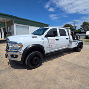 White tow truck parked at a gas station with a clear sky.